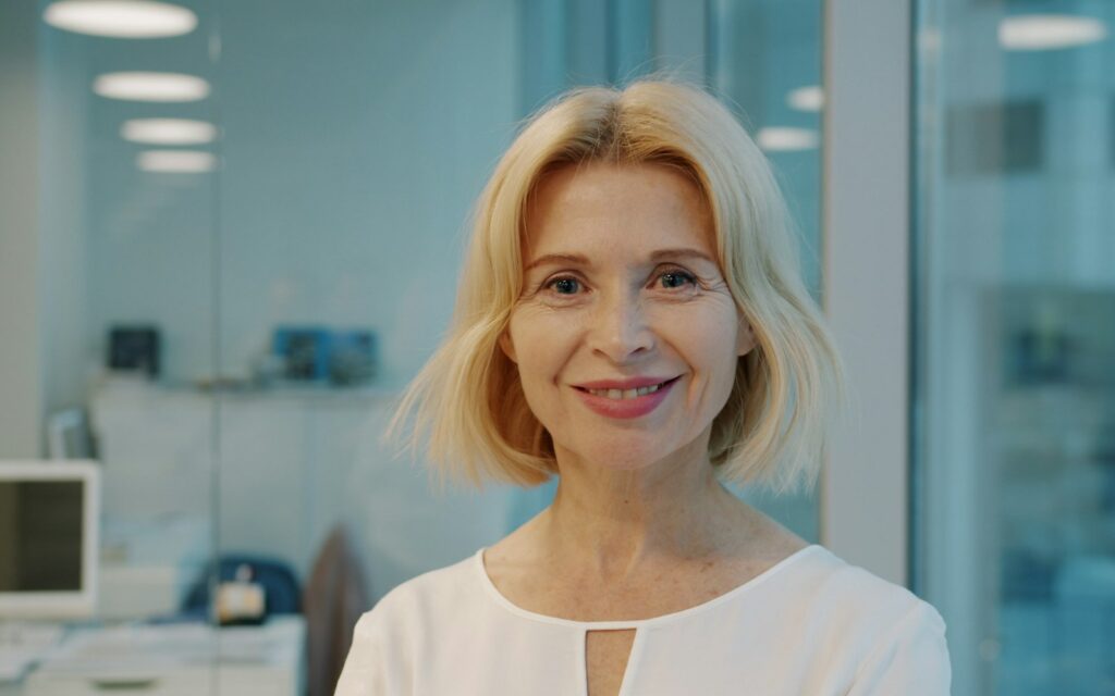 A smiling blonde woman in a white shirt indoors